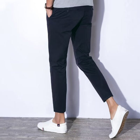 Pantaloni chino neri da uomo, vestibilità slim, abbinati a scarpe bianche casual su pavimento in legno. Moda maschile elegante e moderna.