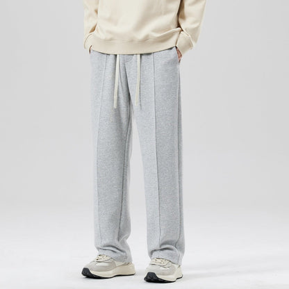Pantaloni tuta grigi da uomo, stile casual, con coulisse, abbinati a felpa beige e sneakers bianche. Moda comoda e moderna.