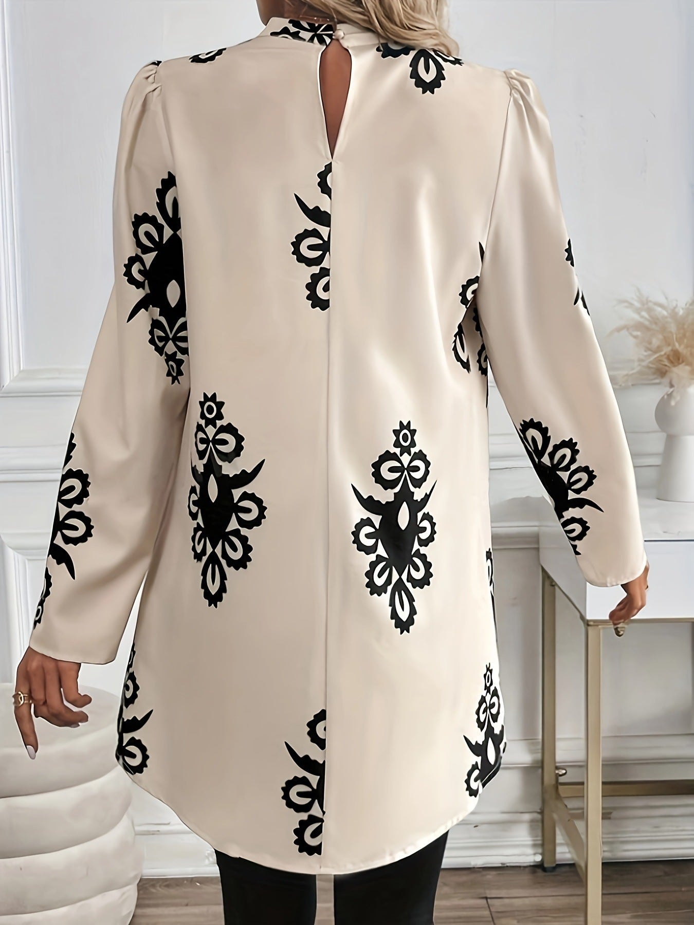 Donna con camicia beige a maniche lunghe con motivi neri, in piedi in una stanza elegante. Moda femminile, abbigliamento autunnale chic.
