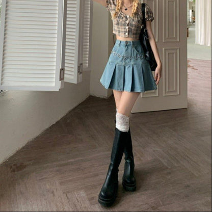Giovane donna in posa con top a quadri e gonna di jeans a pieghe, stivali alti neri e calze bianche, in un ambiente interno moderno.
