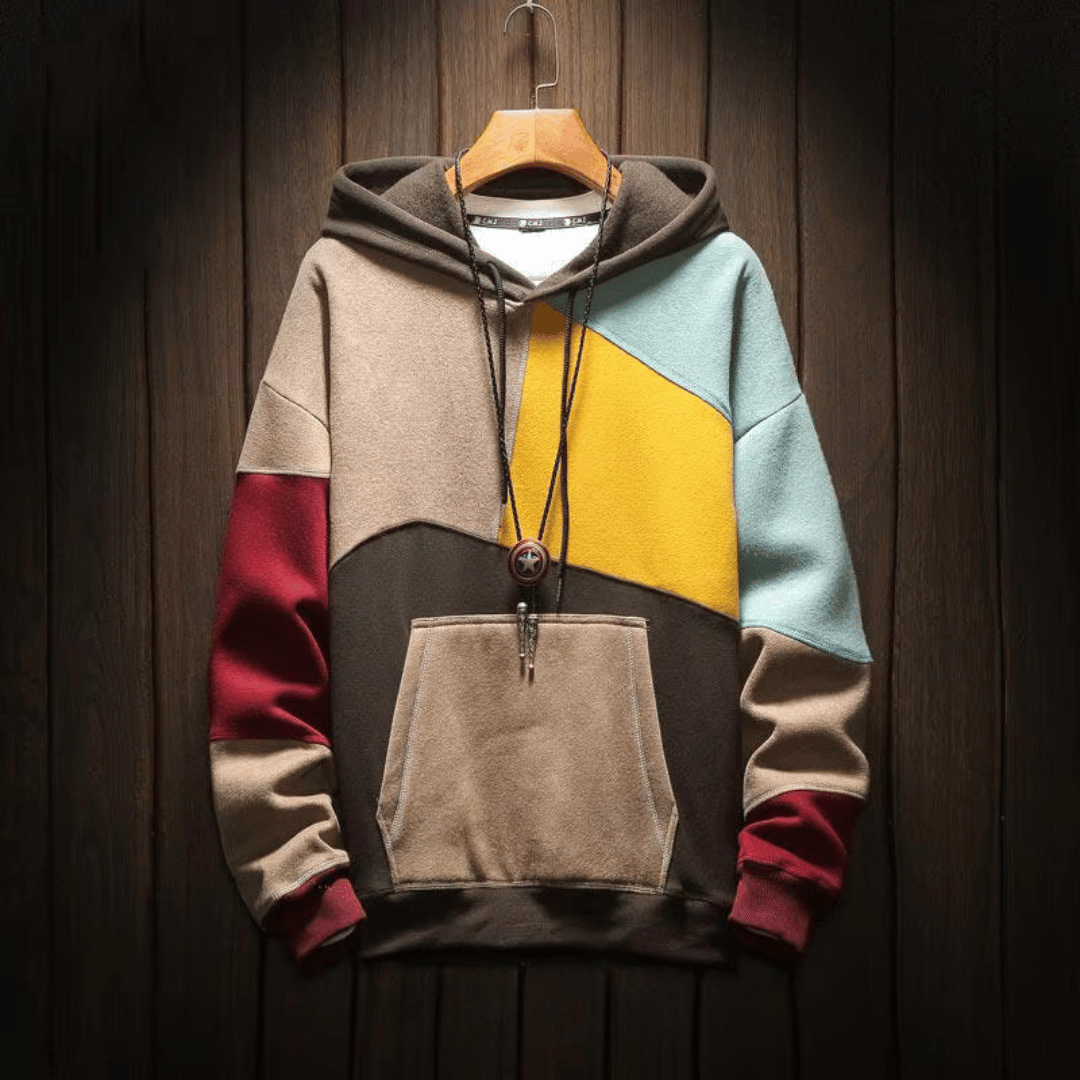Felpa con cappuccio multicolore, design geometrico, tasca frontale, appesa su sfondo in legno. Moda casual, abbigliamento autunnale, stile moderno.