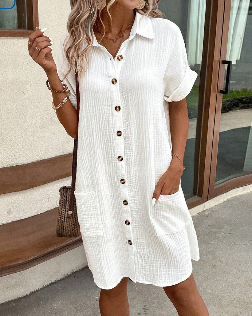 Donna con abito bianco estivo a maniche corte e bottoni, borsa a tracolla marrone, stile casual chic, moda femminile estiva, look elegante.