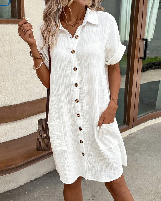 Donna con abito bianco estivo a maniche corte e bottoni, borsa a tracolla marrone, stile casual chic, moda femminile estiva, look elegante.