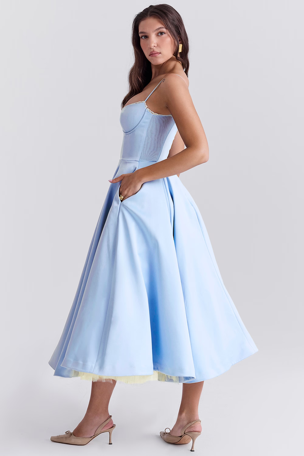 Donna in abito azzurro elegante, stile corsetto, lunghezza midi, con spalline sottili e gonna ampia. Scarpe beige, sfondo neutro. Moda femminile.