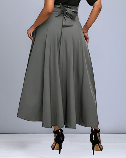 Donna in gonna lunga grigia elegante, vista posteriore, con cintura a fiocco, indossa tacchi alti neri. Moda femminile, abbigliamento chic.