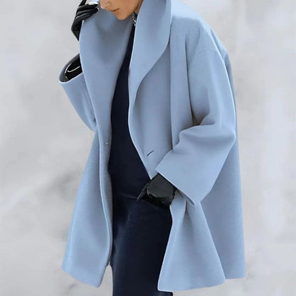 Cappotto oversize azzurro su sfondo neutro, indossato con guanti neri. Moda invernale elegante, stile minimalista, tendenze abbigliamento donna.