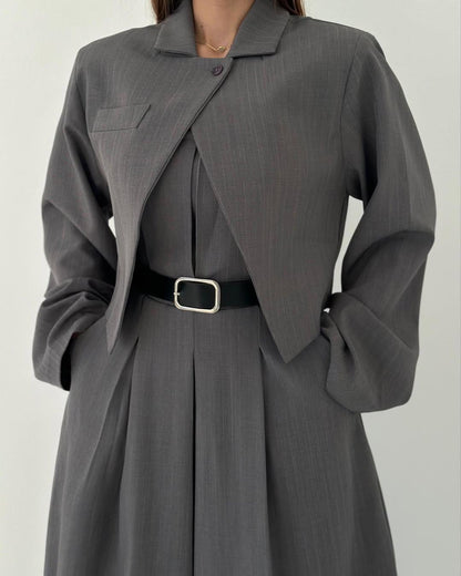 Abito grigio elegante con giacca abbinata, cintura nera con fibbia argentata, indossato da una donna. Moda femminile, stile classico.