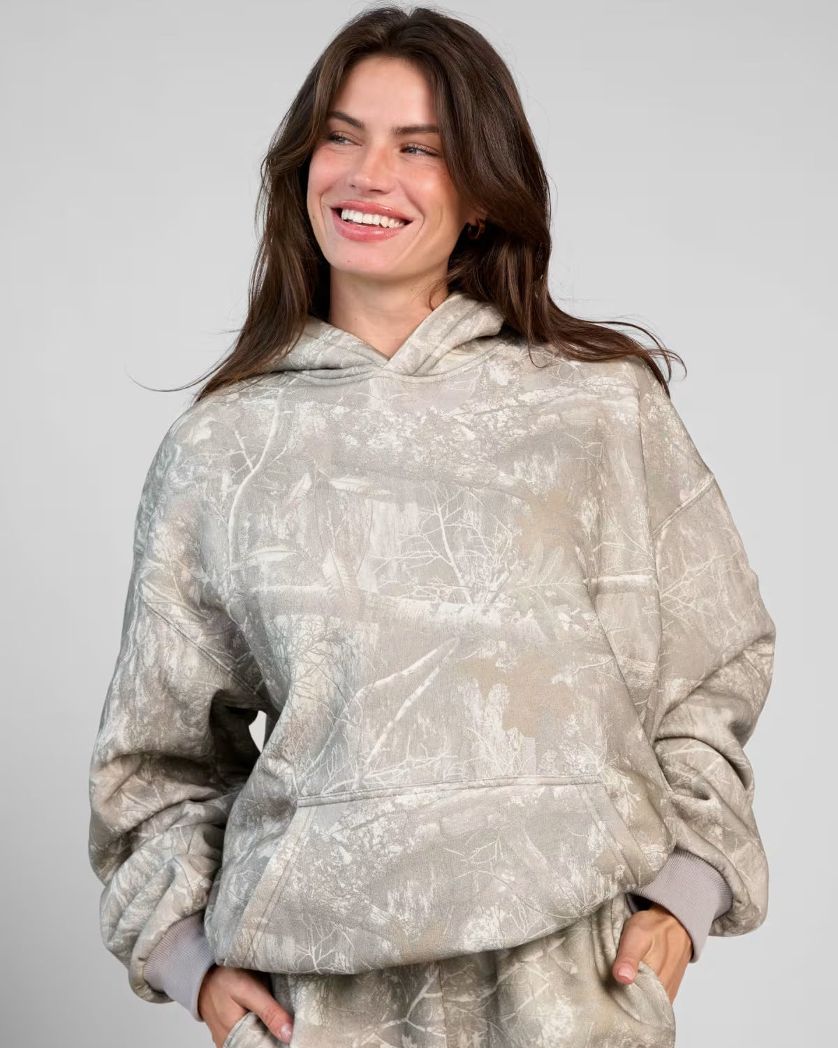 Donna sorridente con felpa con cappuccio grigia a fantasia, moda casual autunno, abbigliamento comodo, stile urbano, sfondo neutro.