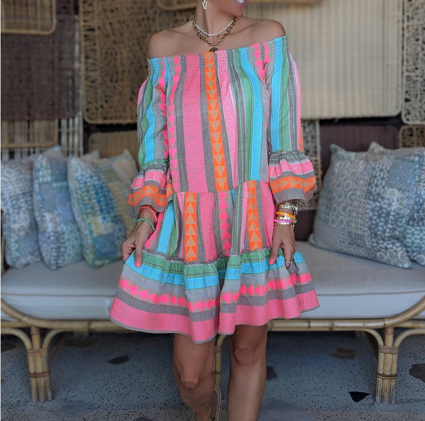 Abito estivo colorato a righe e motivi geometrici, indossato da una donna su un divano in vimini. Moda boho chic, abbigliamento casual estivo.