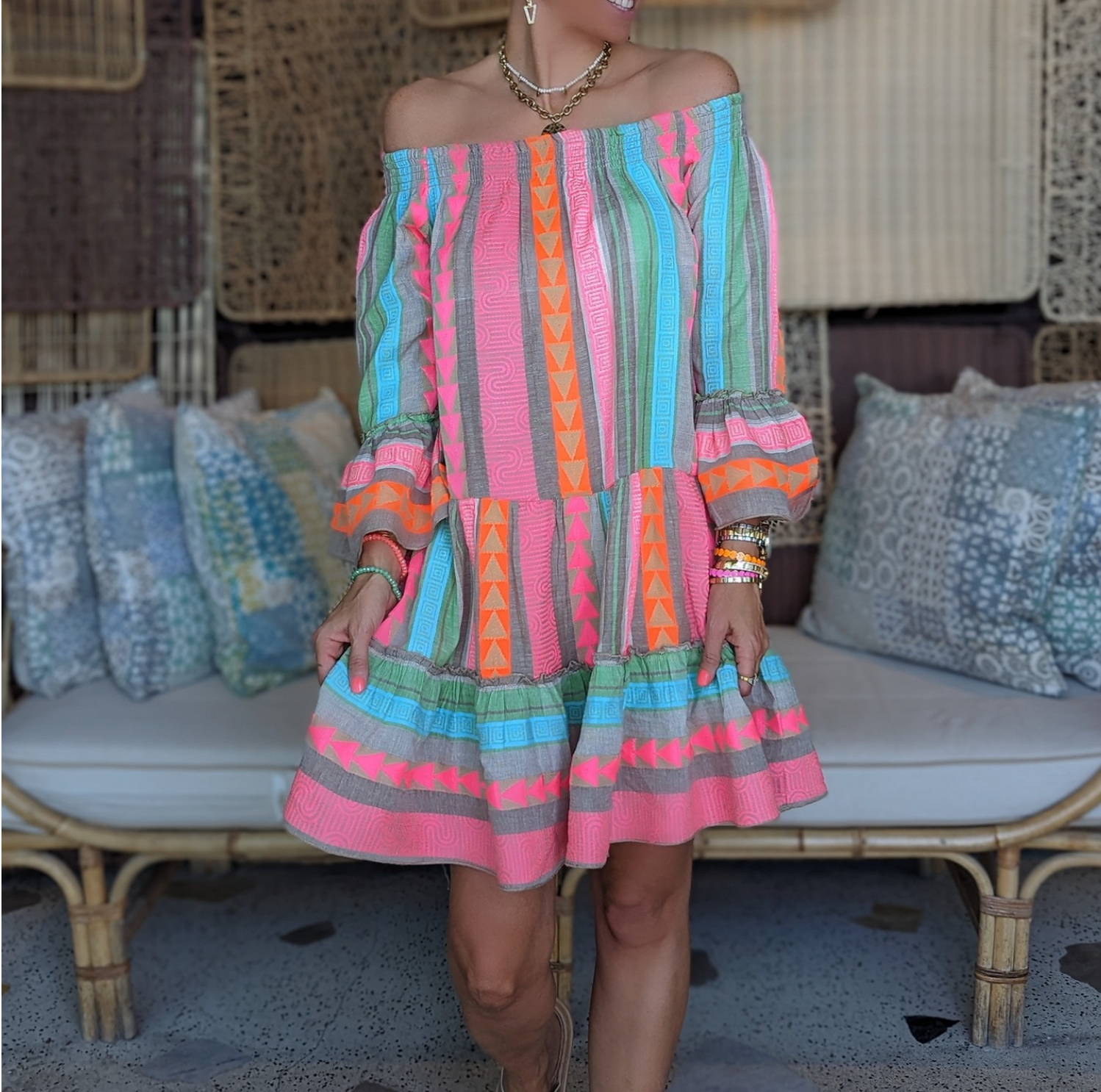 Abito estivo colorato a righe e motivi geometrici, indossato da una donna su un divano in vimini. Moda boho chic, abbigliamento casual estivo.