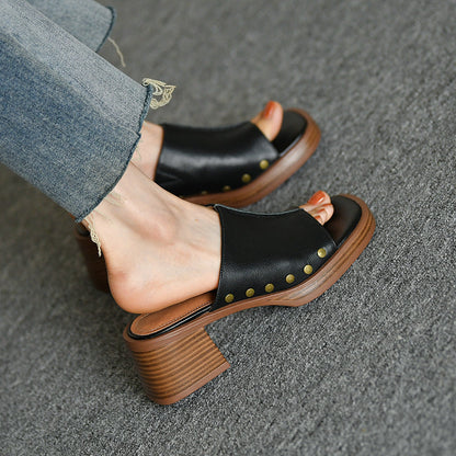 Sandali neri in pelle con tacco largo in legno, dettagli borchiati dorati, indossati con jeans. Scarpe moda donna eleganti e casual.