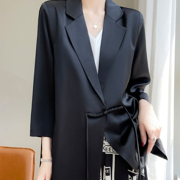 Donna con elegante blazer nero in raso, abbinato a top bianco e pantaloni stampati. Moda femminile, abbigliamento formale, stile sofisticato.