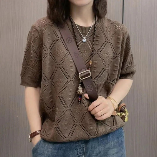 Donna con maglione marrone a maglia traforata, jeans blu, collana e borsa a tracolla. Stile casual, moda autunnale, accessori eleganti.