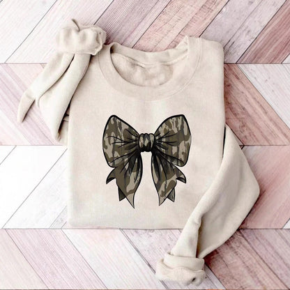 Felpa beige con fiocco stampato in stile mimetico su pavimento in legno chiaro. Moda casual, abbigliamento autunnale, design trendy.