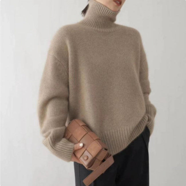 Donna con maglione beige a collo alto, pantaloni neri, borsa intrecciata marrone. Moda autunnale elegante, stile minimalista.