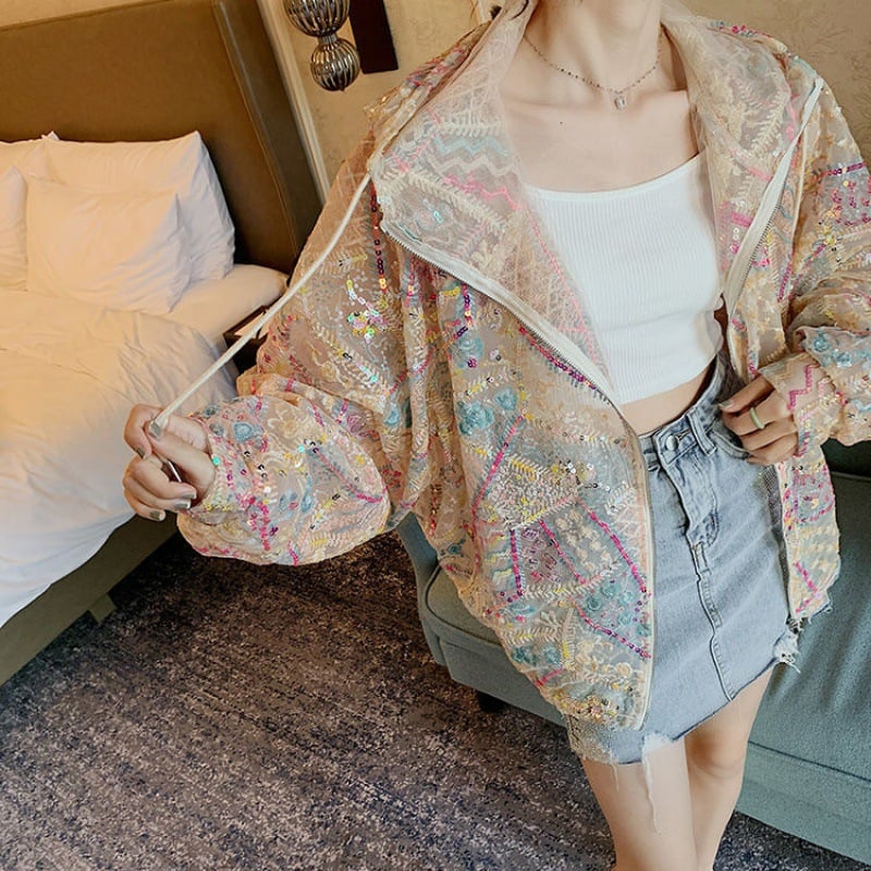 Giacca trasparente ricamata con paillettes colorate, indossata sopra top bianco e gonna di jeans. Stile moda femminile, abbigliamento trendy.