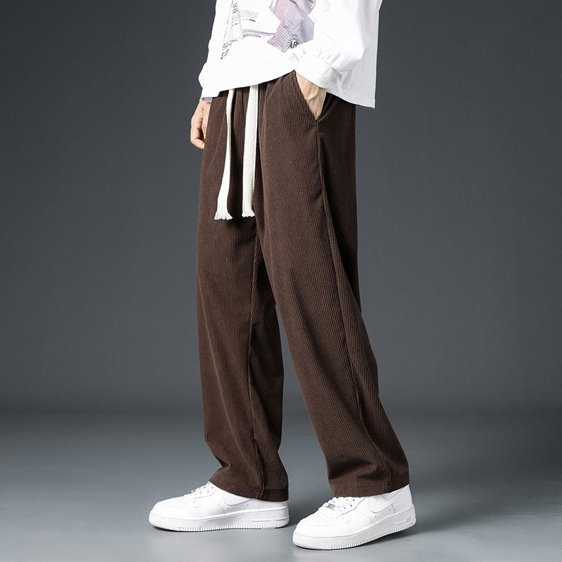 Pantaloni larghi marroni in velluto a coste, indossati con felpa bianca e sneakers bianche, moda casual uomo, stile autunnale.