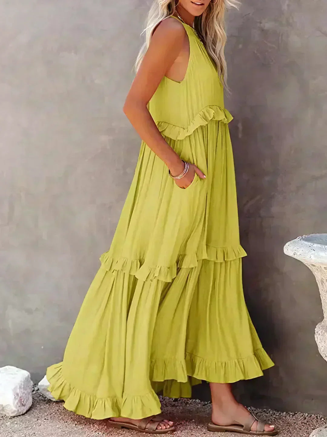 Donna in abito lungo giallo con balze, sandali beige, sfondo grigio. Moda estiva, abbigliamento casual elegante, tendenze abiti femminili.