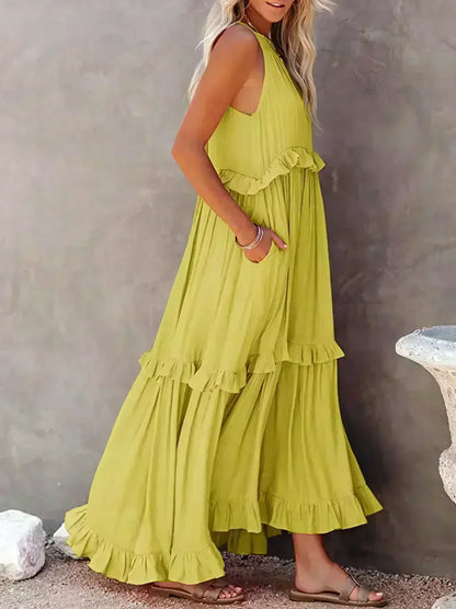 Donna in abito lungo giallo con balze, sandali beige, sfondo grigio. Moda estiva, abbigliamento casual elegante, tendenze abiti femminili.