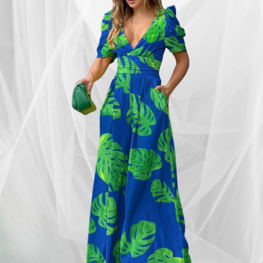 Abito lungo blu con stampa foglie verdi, scollo a V e maniche corte a sbuffo. Donna con borsa verde. Moda estiva elegante e colorata.