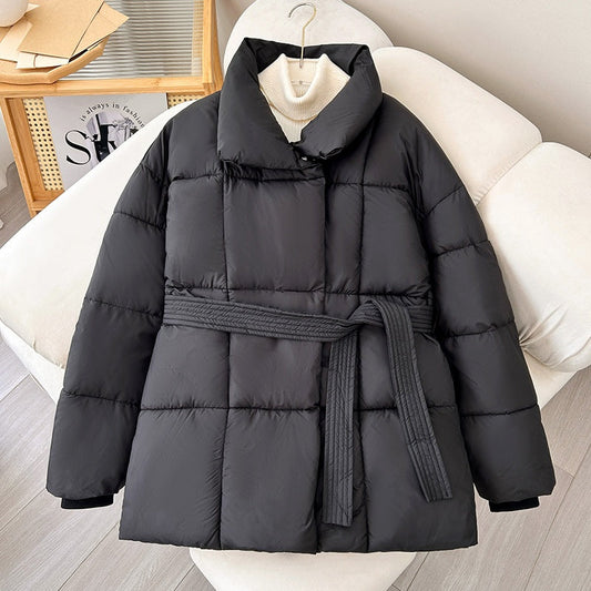 Giacca invernale nera imbottita con cintura, appesa su sedia bianca. Design trapuntato, ideale per moda invernale e abbigliamento caldo.