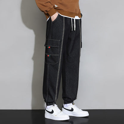 Pantaloni cargo neri da uomo con tasche multiple, cuciture bianche a contrasto, abbinati a scarpe sportive bianche e felpa marrone.