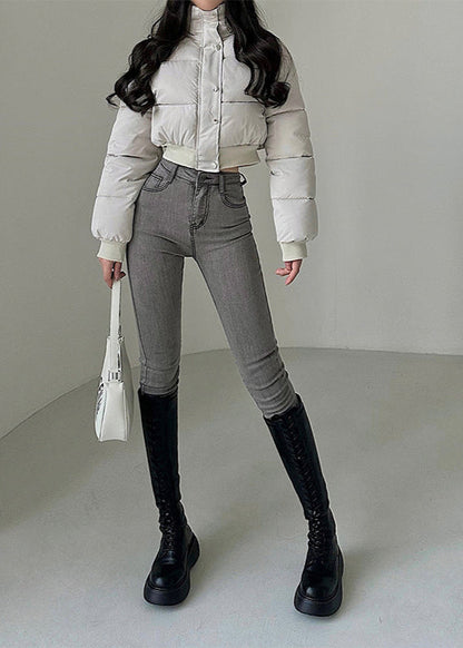 Donna in giacca imbottita bianca, jeans grigi aderenti e stivali neri alti. Moda invernale elegante, outfit casual chic, borsa bianca a mano.