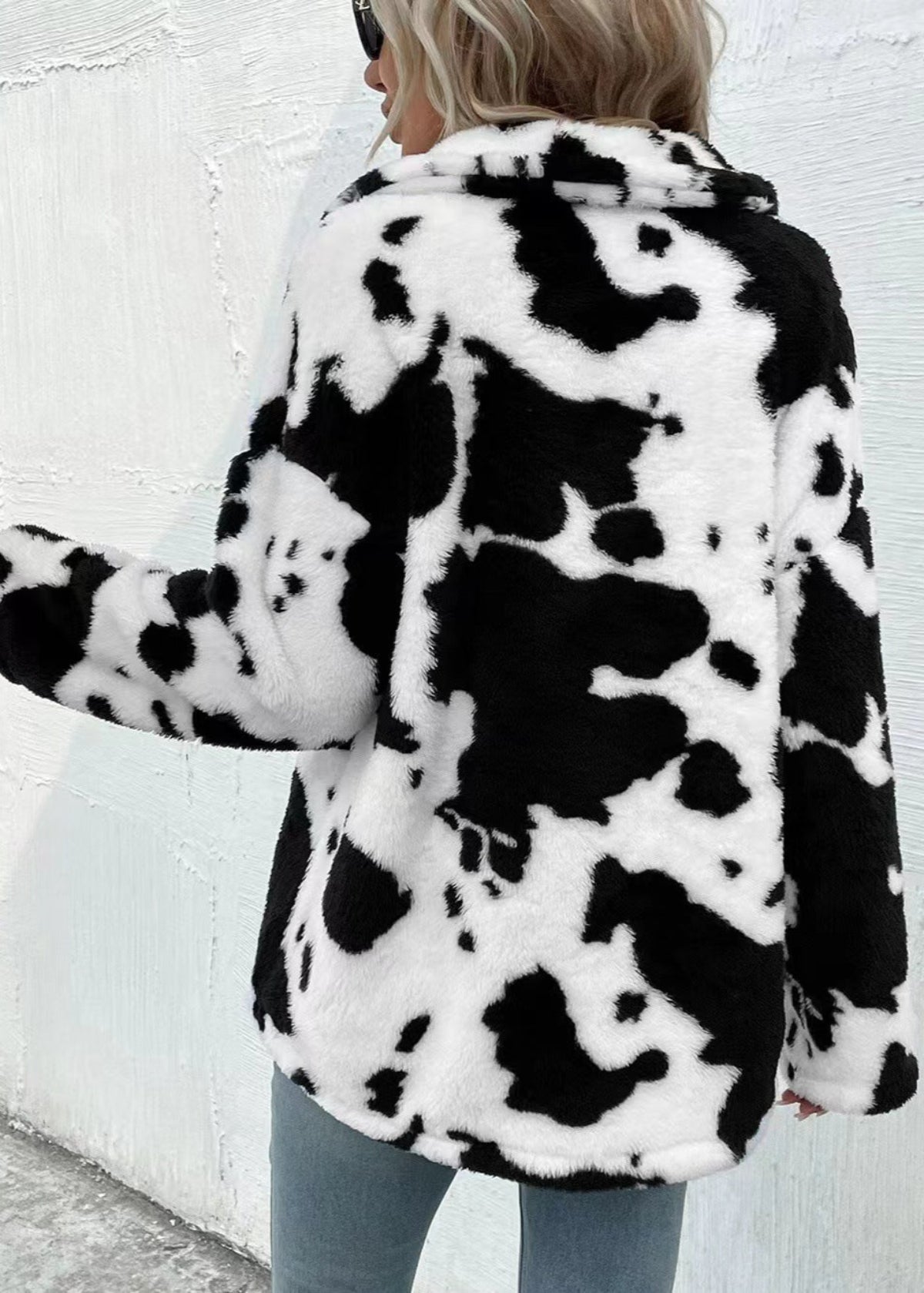 Donna con cappotto in pelliccia sintetica bianco e nero a macchie, stile mucca, di spalle. Moda invernale, tendenza cappotti animalier.