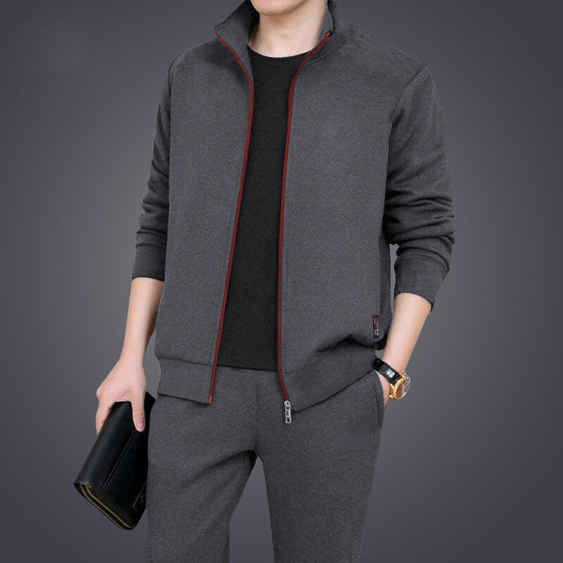 Uomo in tuta sportiva grigia con giacca e pantaloni coordinati, tiene una borsa nera. Abbigliamento casual elegante, moda maschile moderna.