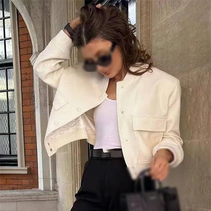 Donna con giacca bianca elegante, top bianco e pantaloni neri, posa con borsa nera. Moda autunnale, stile urbano chic, abbigliamento casual.