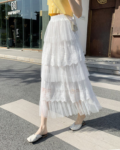 Gonna lunga bianca in tulle a strati con dettagli in pizzo, indossata da una donna su marciapiede urbano. Look estivo elegante e femminile.
