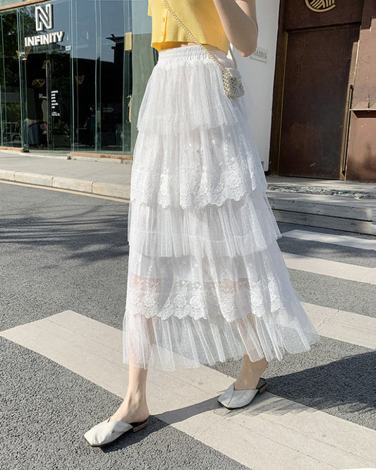 Gonna lunga bianca in tulle a strati con dettagli in pizzo, indossata da una donna su marciapiede urbano. Look estivo elegante e femminile.