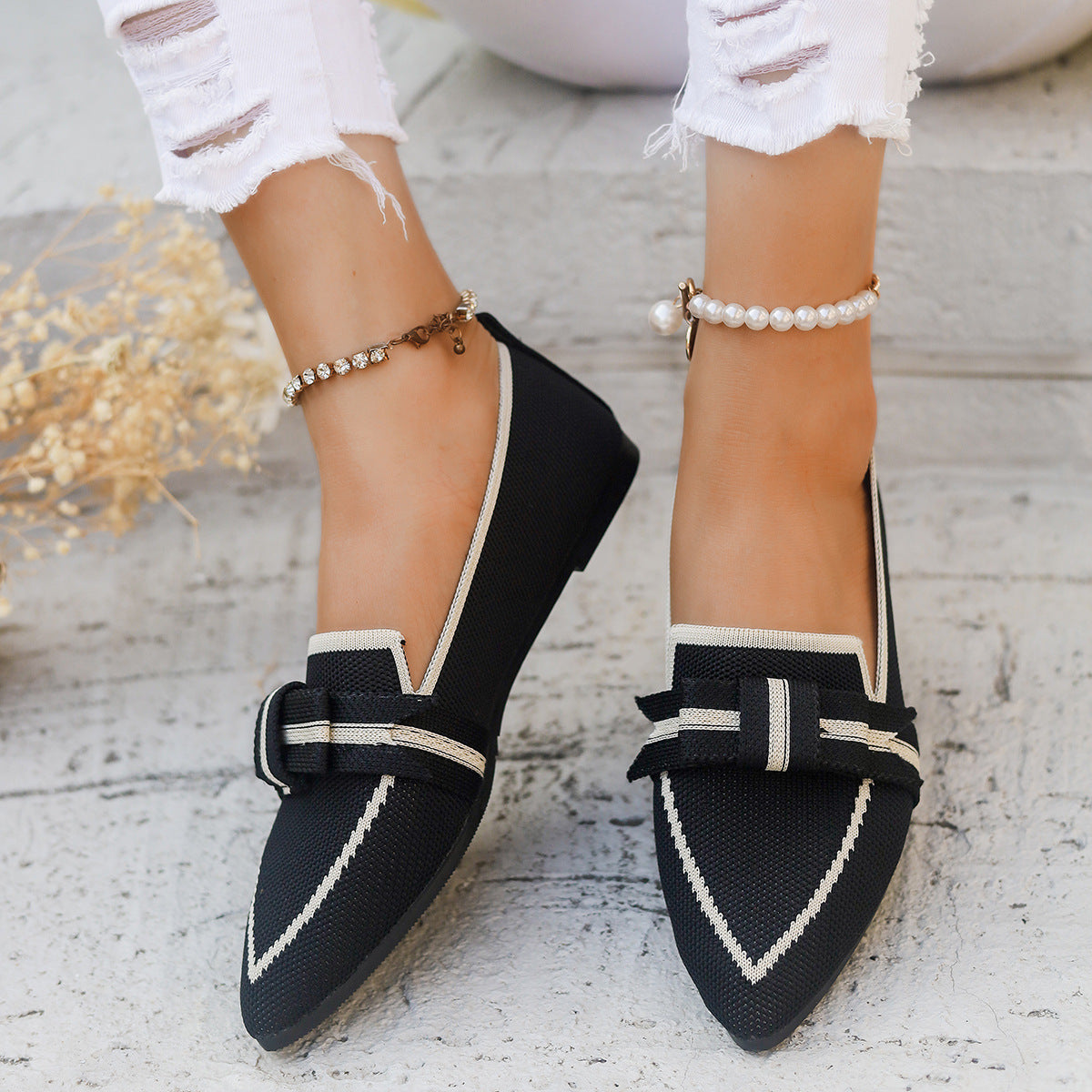 Scarpe mocassini neri da donna con fiocco, indossati con jeans bianchi strappati e cavigliere perle. Eleganza casual, moda femminile.