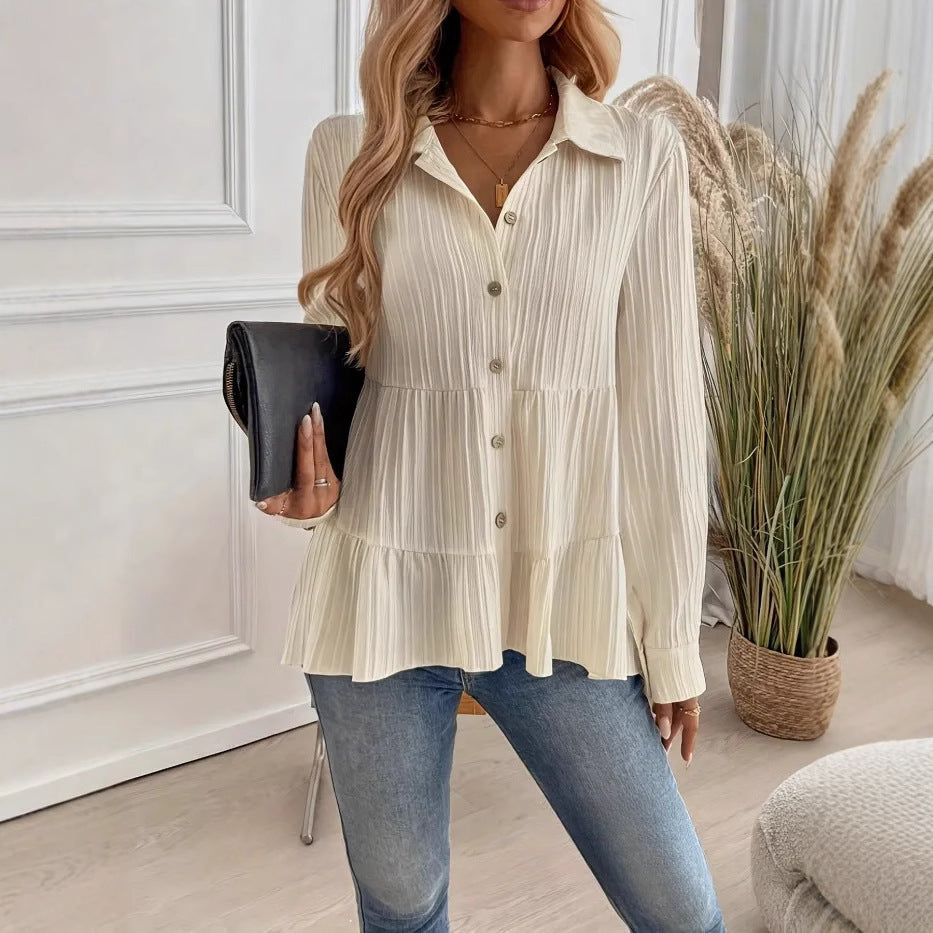 Donna in camicia bianca plissettata, jeans, e borsa nera, in un ambiente moderno con piante decorative. Moda casual elegante, stile autunnale.