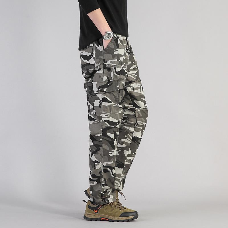 Pantaloni cargo mimetici uomo, tasche multiple, stile militare, abbinati a scarpe trekking marroni, moda casual outdoor.