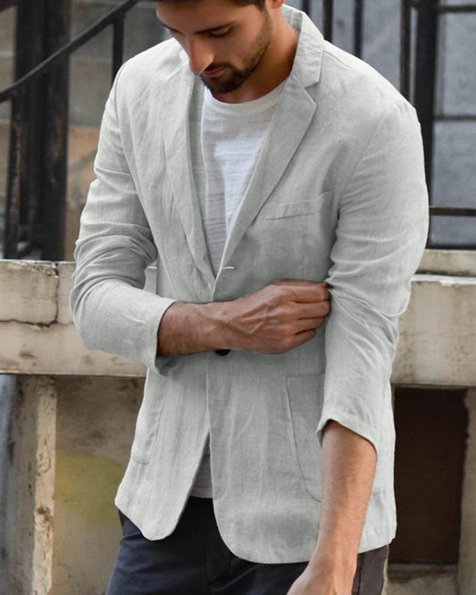 Uomo con giacca di lino grigia, maniche arrotolate, su sfondo urbano. Moda maschile elegante, abbigliamento casual chic.
