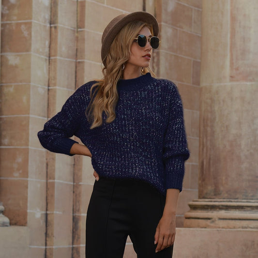 Donna con cappello marrone, occhiali da sole e maglione blu scuro, posa davanti a colonne architettoniche. Moda autunnale, stile urbano elegante.