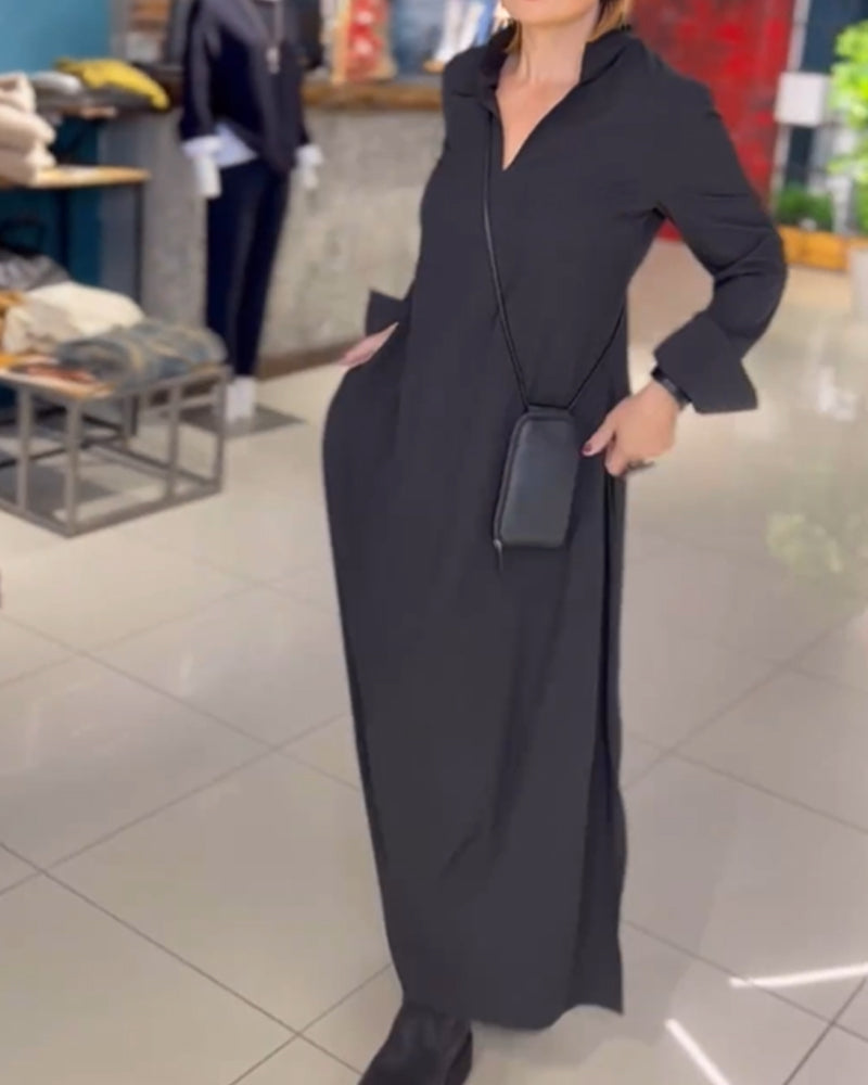 Donna in abito lungo nero con tasche, indossa stivali neri e porta una borsa a tracolla. Sfondo di negozio di abbigliamento.