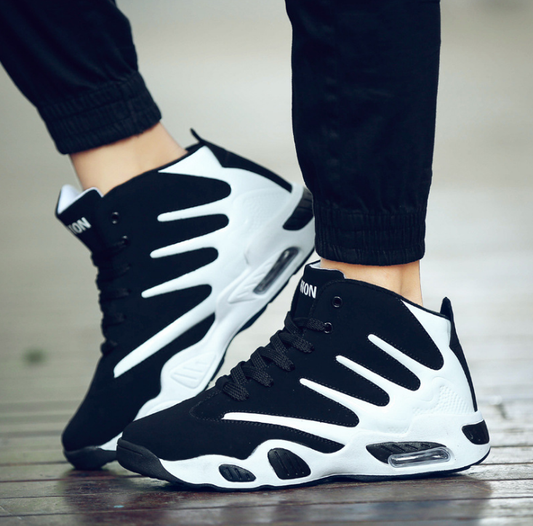Scarpe da ginnastica alte bianche e nere su pavimento in legno, design moderno con suola ammortizzata, ideali per sport e moda urbana.