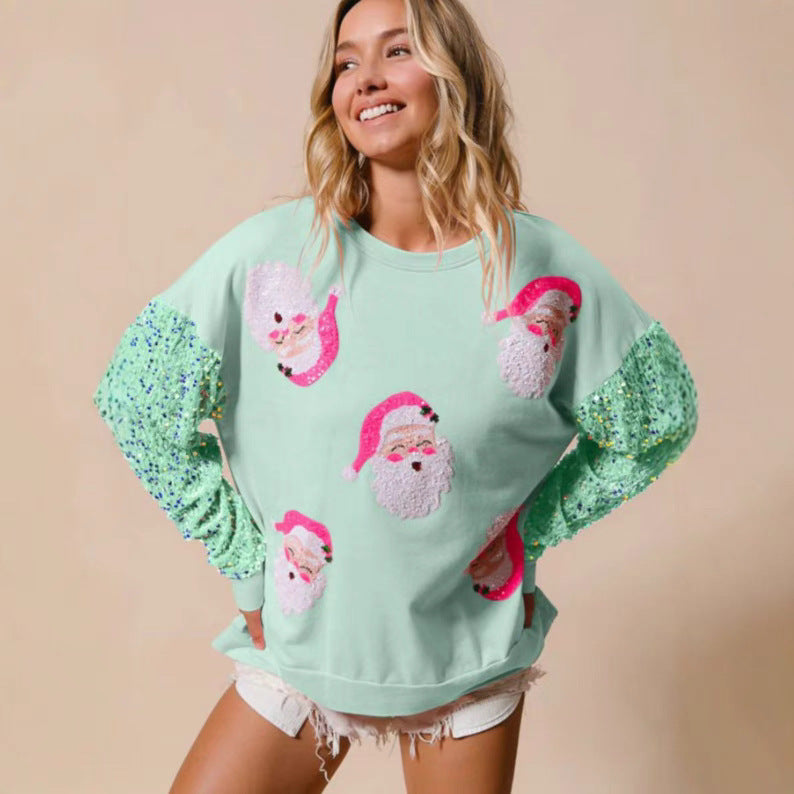 Donna sorridente con maglione verde chiaro natalizio, decorato con facce di Babbo Natale e maniche con paillettes verdi. Moda festiva, abbigliamento natalizio.