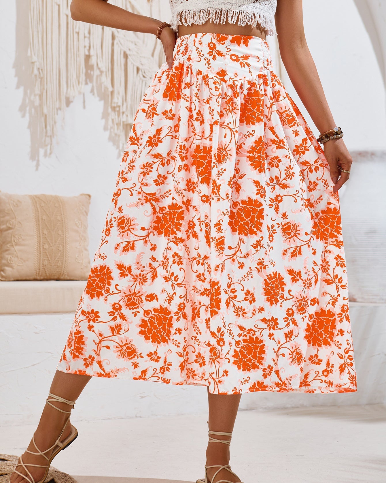 Gonna lunga a fiori arancioni su sfondo bianco, indossata da una donna. Stile boho chic, perfetta per l'estate. Tessuto leggero e decorazioni floreali.