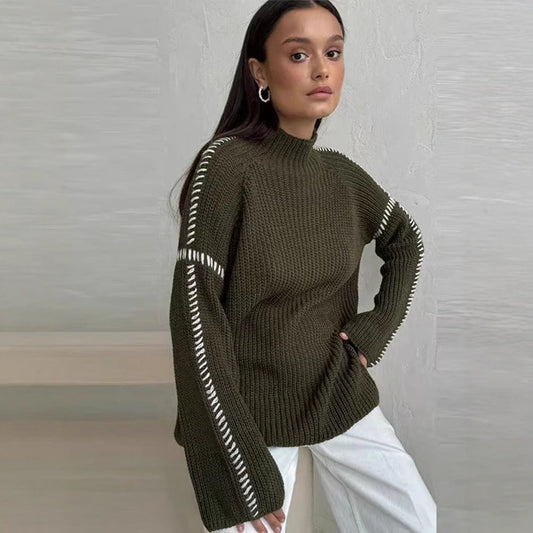 Donna con maglione verde oliva a maglia grossa, dettagli bianchi sulle maniche, posa elegante. Moda autunnale, stile casual chic.