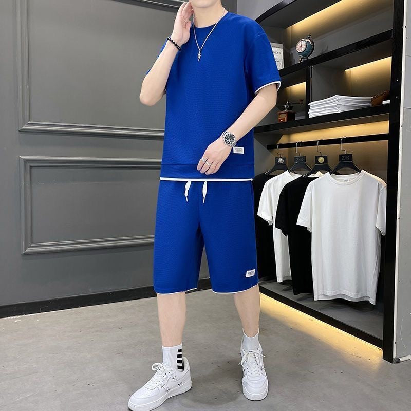 Uomo in tuta sportiva blu, scarpe bianche, orologio al polso, in negozio di abbigliamento moderno con magliette appese. Moda casual maschile.