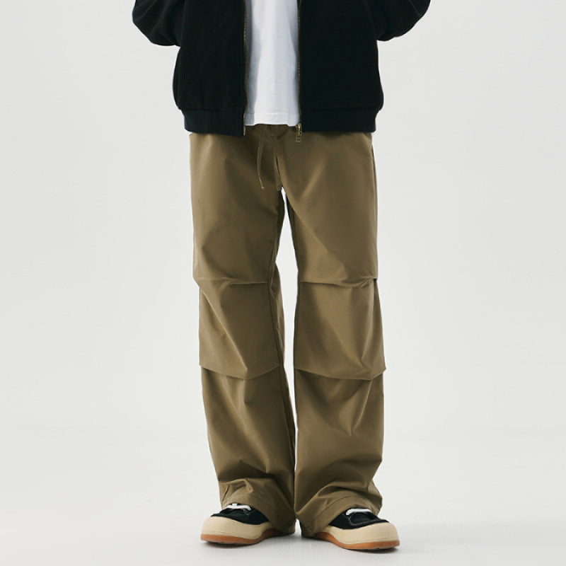 Pantaloni cargo beige da uomo, stile casual, con tasche multiple, abbinati a giacca nera e scarpe sportive. Moda streetwear contemporanea.
