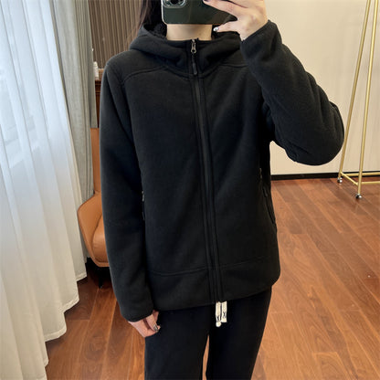 Donna indossa giacca nera con cappuccio, zip frontale, in una stanza moderna con pavimento in legno. Moda casual, abbigliamento invernale, stile urbano.