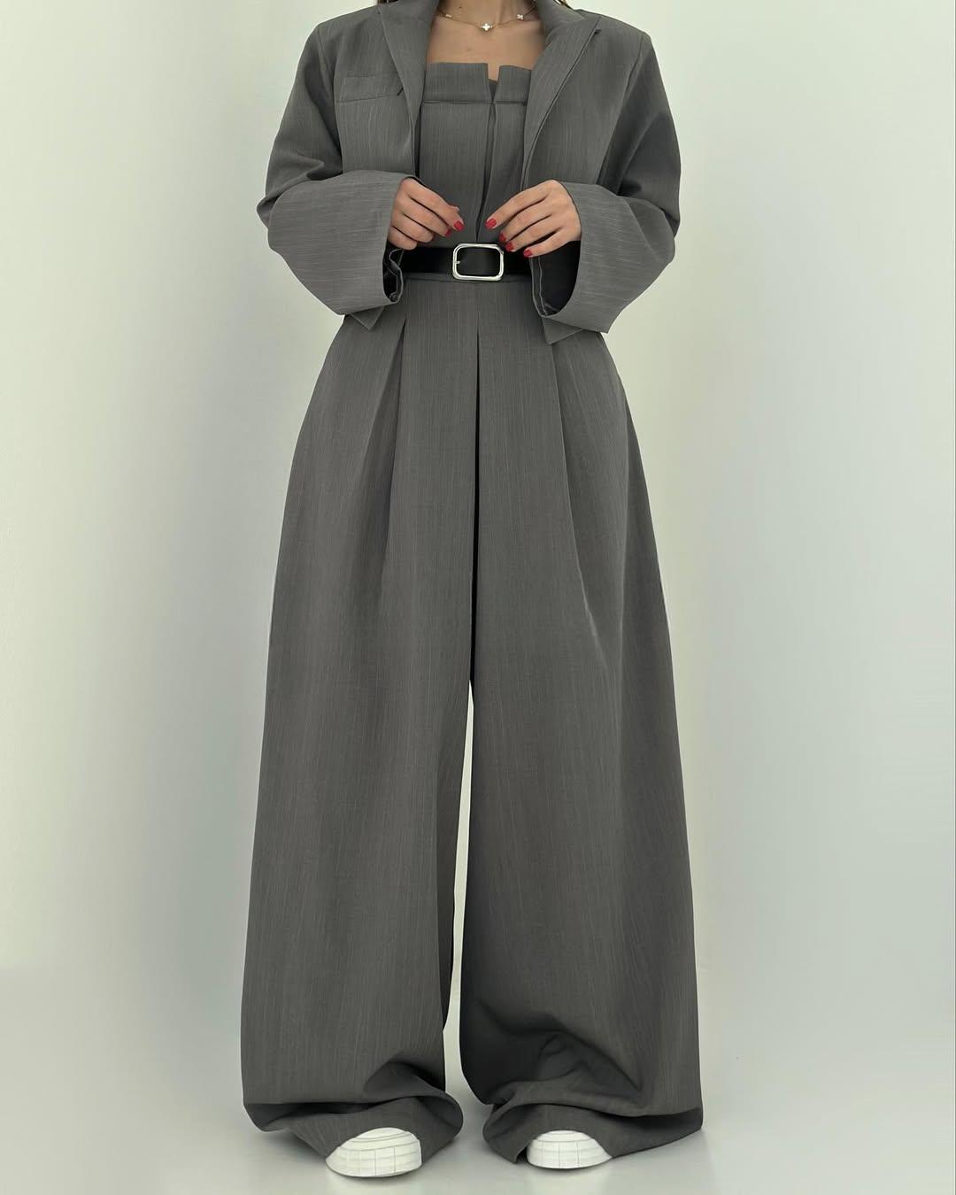 Tuta elegante grigia con cintura nera, giacca abbinata e scarpe bianche. Moda donna, abbigliamento formale, stile contemporaneo.