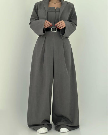 Tuta elegante grigia con cintura nera, giacca abbinata e scarpe bianche. Moda donna, abbigliamento formale, stile contemporaneo.