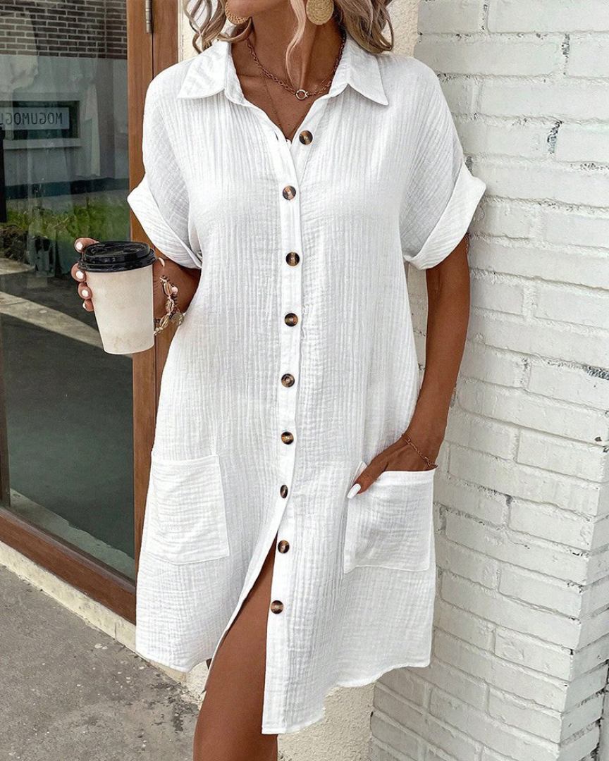 Donna con abito camicia bianco estivo, bottoni in legno, tasche frontali, sorseggia caffè. Moda casual, look estivo, abbigliamento femminile.