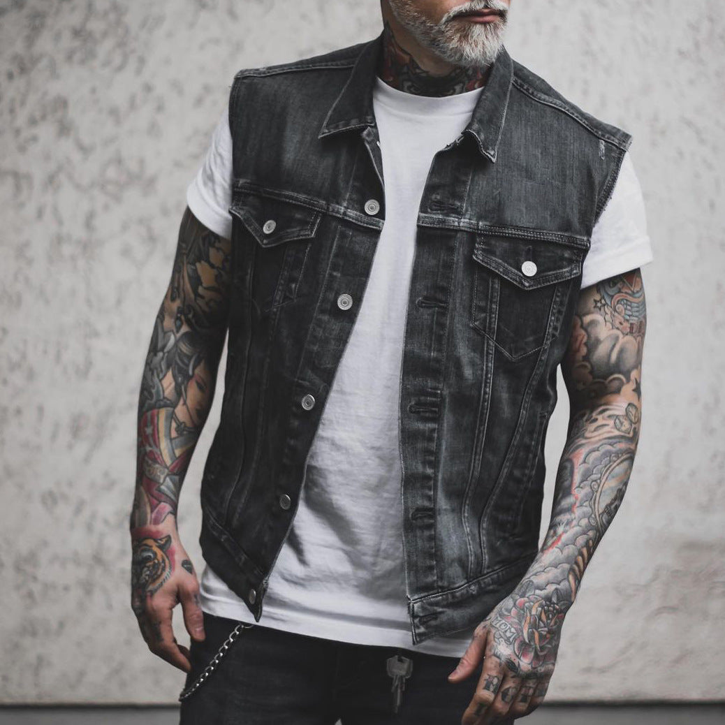 Giacca di jeans nera senza maniche su uomo tatuato, indossa maglietta bianca. Moda streetwear, stile casual, tendenze abbigliamento maschile.