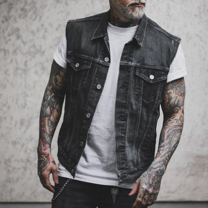 Giacca di jeans nera senza maniche su uomo tatuato, indossa maglietta bianca. Moda streetwear, stile casual, tendenze abbigliamento maschile.